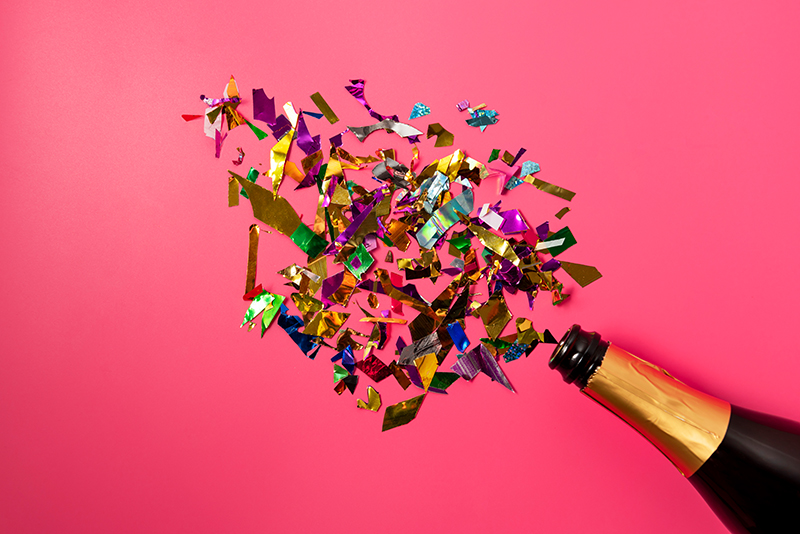 Champagne bottle with confetti on pink background. Flat lay.